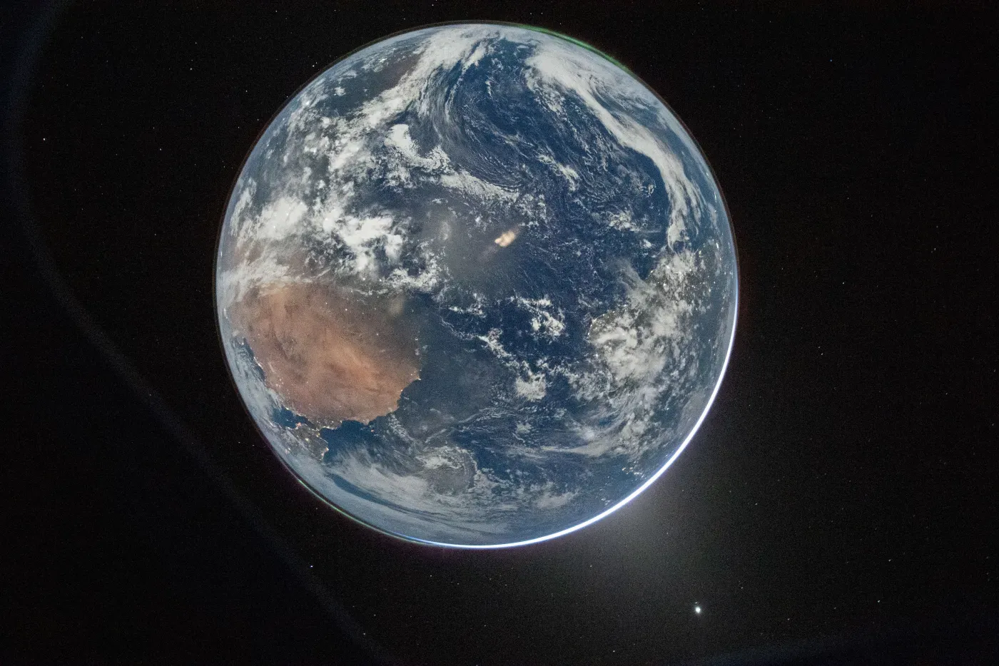 A full view of Earth against black space—blue oceans, white cloud, the tan of Africa and Madagascar—seen from the outbound Artemis II spacecraft.