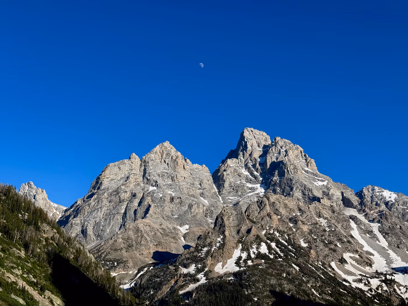 Mountain peaks at dusk with the moon directly above them.