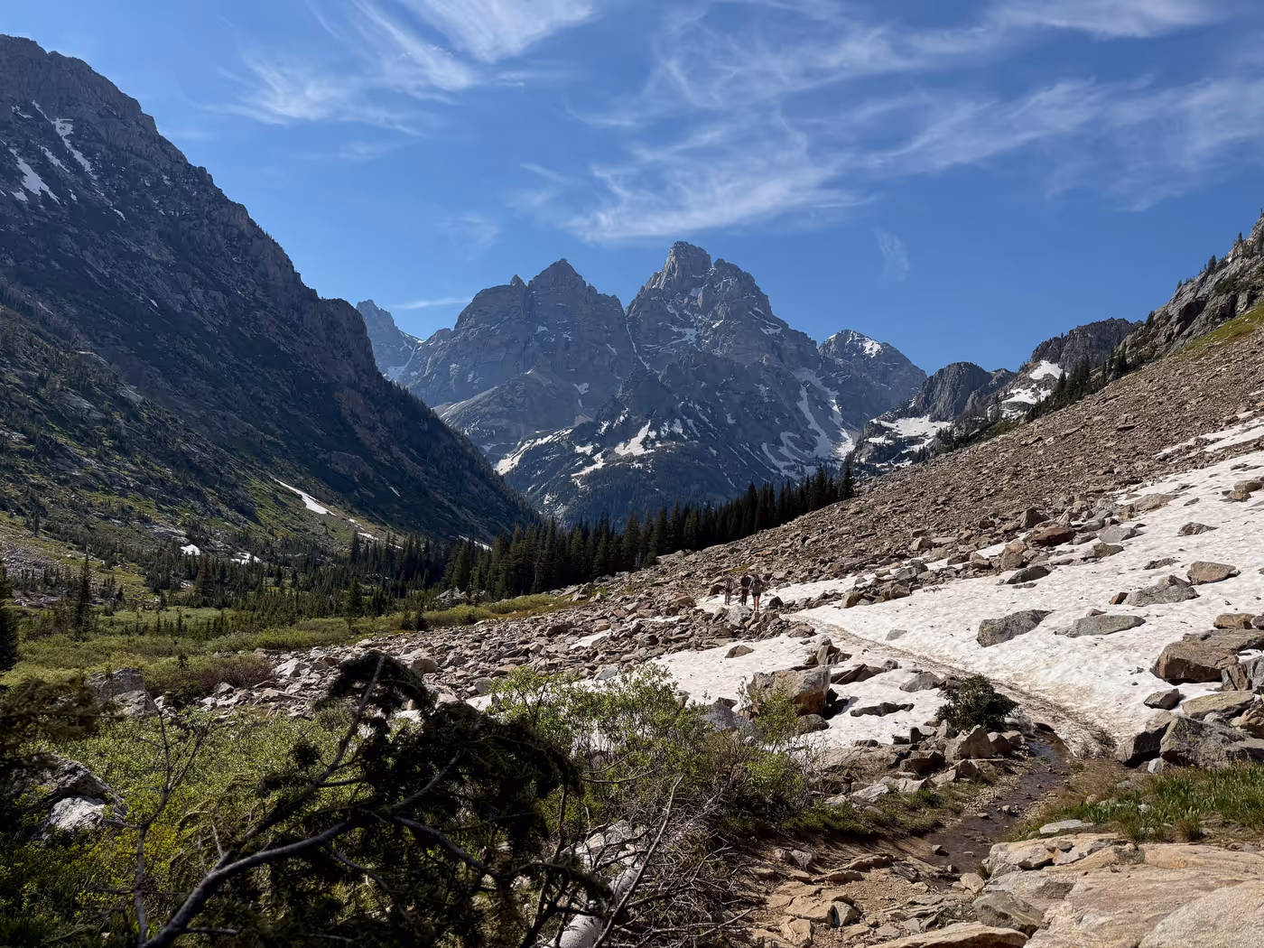 Hikers ascending a snow- and slush-covered trail up a canyon toward a high alpine basin.