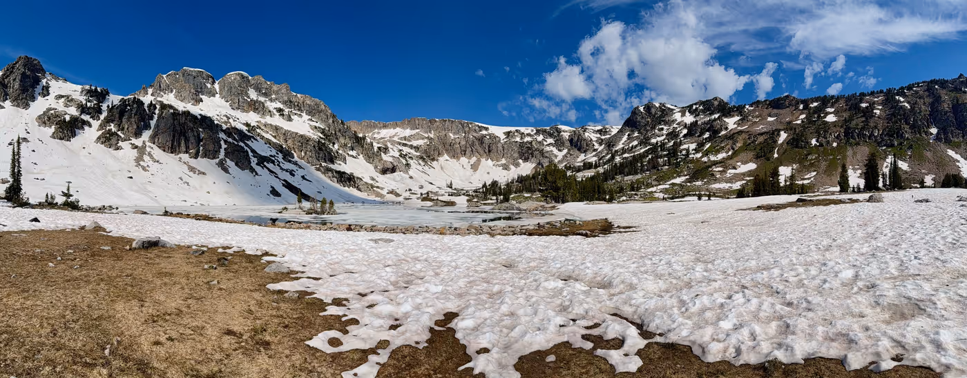 A clear alpine lake with floating ice and snowbanks, peaks behind.