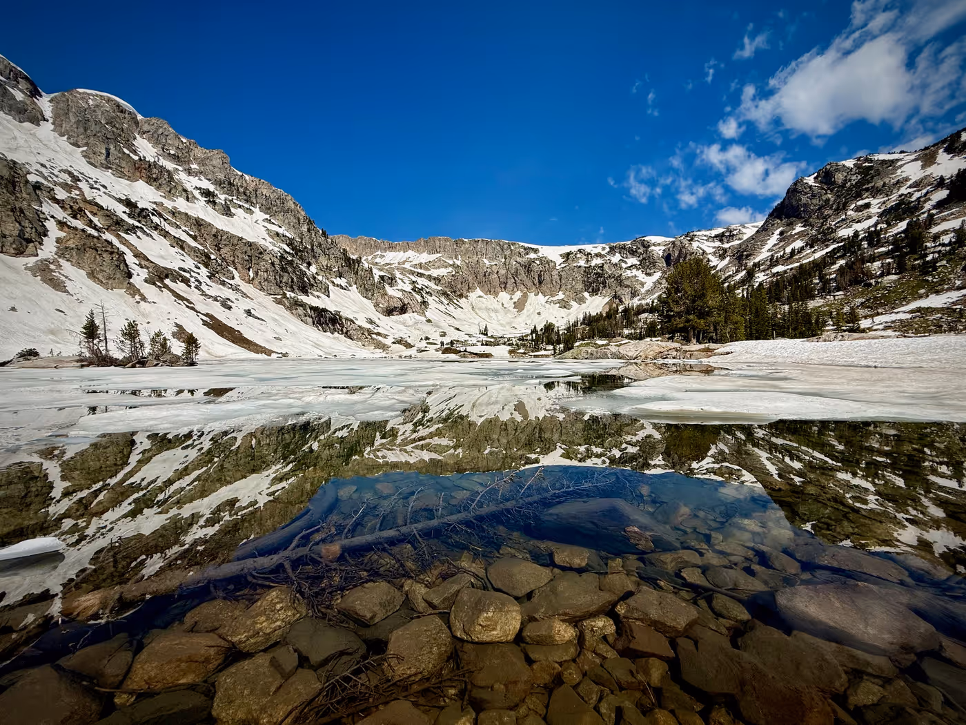 Clear shallow lake water over rock, with snow patches at the shore.