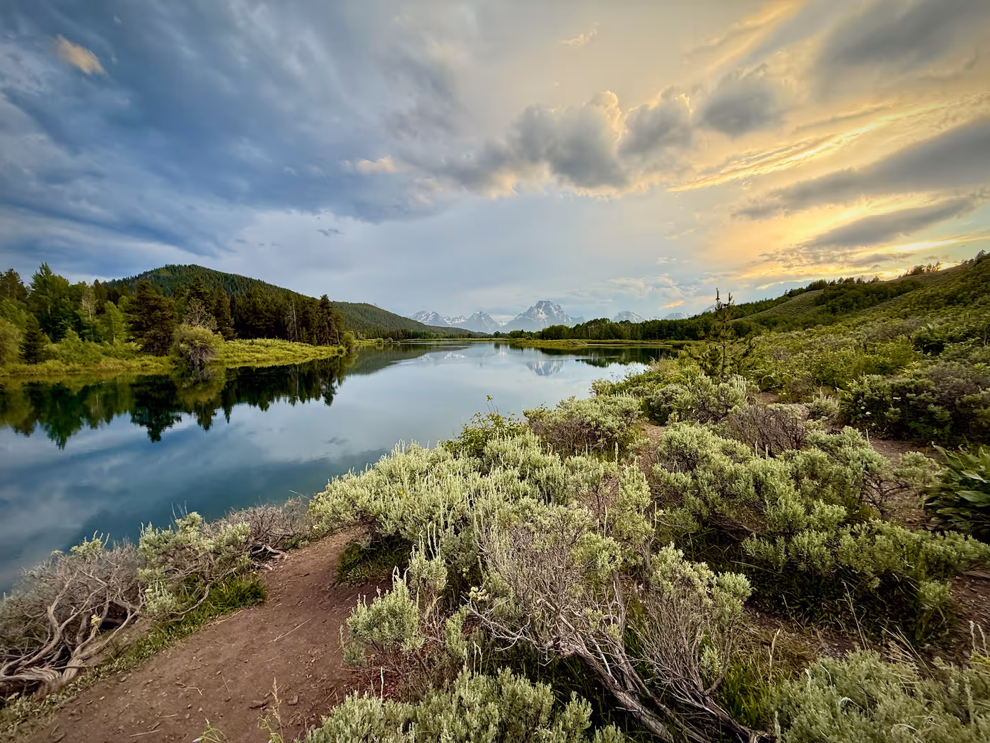 A still river bend at sunset with mountains behind.
