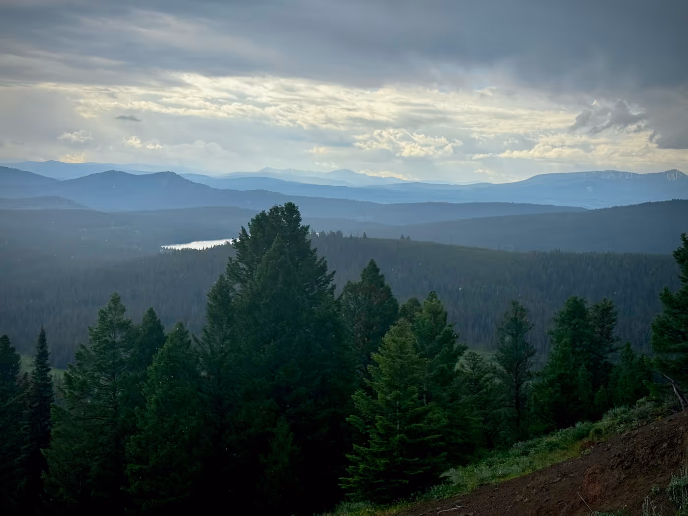 A forested valley and distant ranges under heavy storm clouds.
